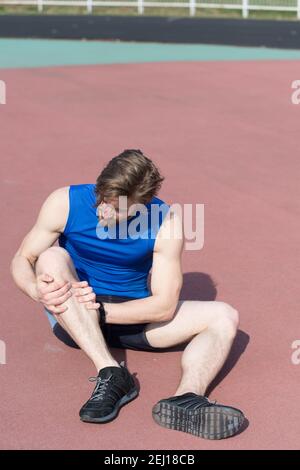 Verletzten Läufer, bärtiger Mann oder Mann mit athletischen Körper auf der Laufstrecke Gefühl Schmerz der gebrochenen Bein sonnige in blau Sportbekleidung. Sommer Aktivität, Sport. gesunder Lebensstil und Workout. sport Trauma Stockfoto