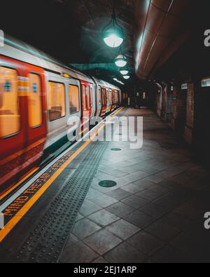 London UK Januar 2021 U-Bahn London U-Bahn nähert sich dem Bahnsteig, verschwommen in Bewegung mit langer Belichtung. Vertikale dunkle launische Aufnahme Stockfoto