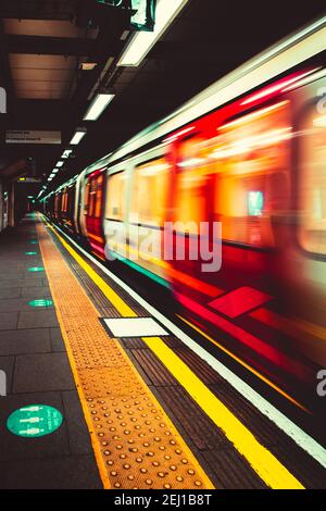 London UK Januar 2021 U-Bahn London U-Bahn nähert sich dem Bahnsteig, verschwommen in Bewegung mit langer Belichtung. Vertikale dunkle launische Aufnahme Stockfoto