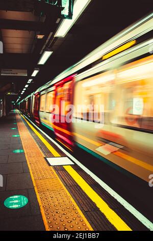 London UK Januar 2021 U-Bahn London U-Bahn nähert sich dem Bahnsteig, verschwommen in Bewegung mit langer Belichtung. Vertikale dunkle launische Aufnahme Stockfoto