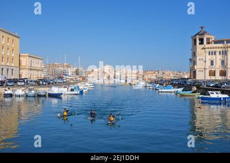 SIRACUSA, ITALIEN - JENUARY 17: Fischerboote und Kajakfahrer in der darsena der Ortigia Insel von der Brücke Umbertino. Im Hintergrund die Skyline von S Stockfoto