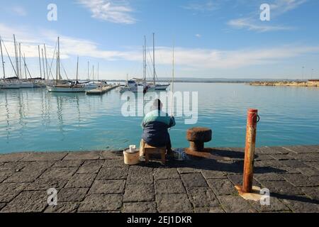 SIRACUSA, ITALIEN - JENUARY 03: Rückansicht des Mannes, der auf dem Pier von Ortigia sitzt und angeln, Altstadt von Siracusa. Sizilien. Aufgenommen 2015 Stockfoto