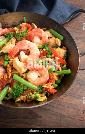 Meeresfrüchte-Gericht mit Reis, Garnelen, Hühnerfleisch und Gemüse in einer kleinen Paella-Pfanne auf einem dunklen rustikalen Holztisch, ausgewählte Fokus, enge Schärfentiefe Stockfoto