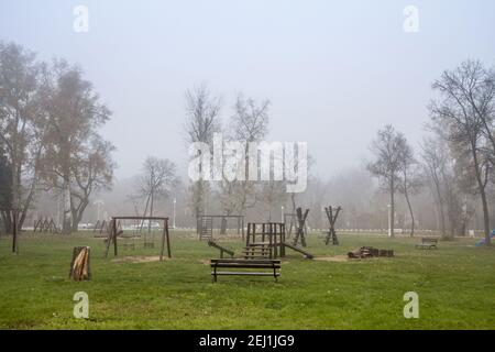 Hölzerner Kinderspielplatz, ein Spielplatz aus Rutschen und Schaukeln, leer, in einem geheimnisvollen nebligen Smog, während eines kalten Winters oder Herbstnachmittag. P Stockfoto