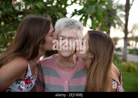 Eine Großmutter bekommt während des National Grosselters Day einen Kuss auf die Wangen von ihren Enkeltöchtern und sie ist sehr glücklich. Stockfoto