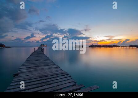 Sonnenuntergang auf Mabul Island mit Holzsteg, seidigem Wasser und schwimmendem Haus. Stockfoto