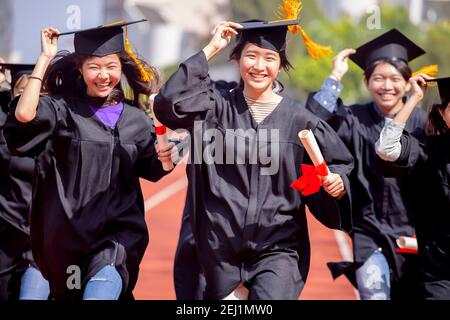 Glückliche Abschlussstudenten mit Diplom und laufen auf dem Stadion In der Schule Stockfoto