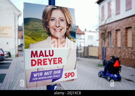 04. Februar 2021, Rheinland-Pfalz, Haßloch: Ein Mann im elektrischen Rollstuhl fährt an einem Wahlplakat vorbei, das dem Ministerpräsidenten von Rheinland-Pfalz und Spitzenkandidaten der SPD für die anstehenden Landtagswahlen in Gestalt von Malu Dreyer ähneln soll. (Zu dpa: 'Was macht Hassloch ticken? - Vorwahlstimmung in Mini-Deutschland in der Pfalz') Foto: Uwe Anspach/dpa Stockfoto