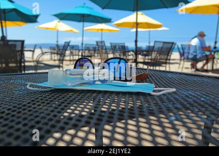 Sonnenbrille, Hand-Desinfektionsmittel und Gesichtsmaske auf dem Cafe-Tisch Stockfoto