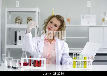 Junge blonde Wissenschaftler vergleichen die Ergebnisse neuer chemischer Forschung mit experimentellen Diagrammen auf dem Clipboard. Arbeitsatmosphäre in chemischer l Stockfoto