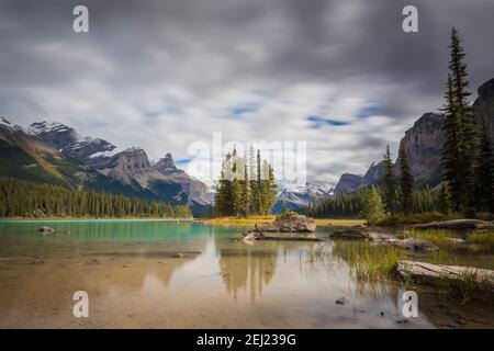 Lange Exposition Landschaft der Rocky Mountains reflektiert auf klaren grünen See Wasser mit Fichten und Pinien unter einem bewölkten Himmel, Jasper, Kanada Stockfoto