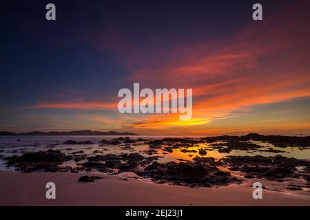 Tropischer Sommer Sonnenuntergang Landschaft am Strand mit Sand, Felsen, Wasser, ruhiges Meer, bunter blauer Himmel mit orangen Wolken, Guanacaste, Costa Rica Stockfoto