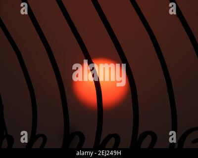 Selektive Fokus von Metall rustikalen Bars gegen den verschwommenen Himmel und Sonne während des Sonnenuntergangs, Silhouette Ansicht, Sonne hinter Bars Stockfoto