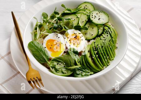 Quinoa-Schüssel mit Ei, Sonnenblumengemüse, Gurke, Avocado, Babyspinat in einer weißen Schüssel auf einem weißen Holztisch, Nahaufnahme, türkische Küche Stockfoto