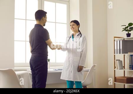 Ärztin begrüßt und schüttelt die Hände mit männlichen Patienten während der Sitzung in der medizinischen Praxis. Stockfoto