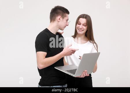 Zwei Teenager Kerl und Mädchen sind mit Laptop und emotionsgeladen diskutieren etwas auf weißem Hintergrund im Studio. Stockfoto