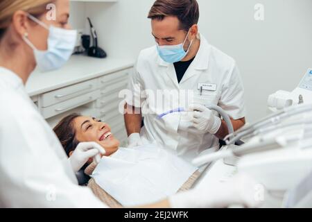Frau lächelt während ihrer zahnärztlichen Behandlung beim Zahnarzt. Zahnärzte, die eine Patientin im Krankenhaus behandeln. Stockfoto