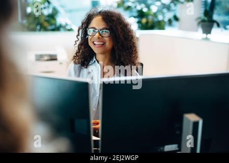 Lächelnde Frau, die an der Rezeption eines Gemeindeamtes arbeitet. Eine Dame, die hinter dem Schreibtisch saß und lächelte und eine Frau ansah. Stockfoto