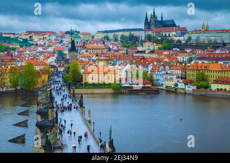 Bewundernswerter Blick auf die Stadt mit der berühmten Promenade auf der Karlsbrücke. Touristen mit bunten Regenschirmen zu Fuß in regnerischen Tag, Prag, Tschechische Republik, E Stockfoto