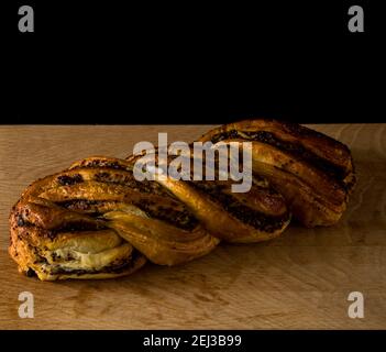 Geflochtenes Brötchen mit Mohnsamen, Gebäck, auf einem Holzbrett auf schwarzem Hintergrund Stockfoto