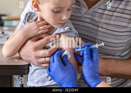 Ein kleines Mädchen mit ihrem Vater in der Arztpraxis der Klinik wird gegen das Coronavirus geimpft. Das Konzept der Impfung, immunizati Stockfoto