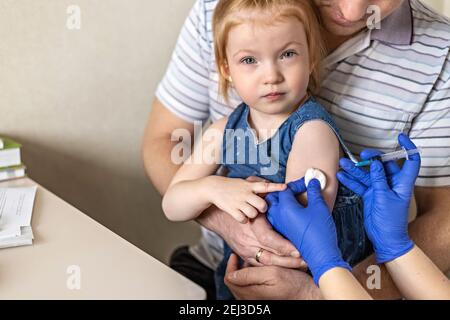 Ein kleines Mädchen mit ihrem Vater in der Arztpraxis der Klinik wird gegen das Coronavirus geimpft.das Konzept der Impfung, Immunisierung Stockfoto