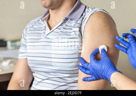 Ein Arzt impft einen Mann gegen Coronavirus in einer Klinik. Nahaufnahme. Das Konzept der Impfung, Immunisierung, Prävention gegen Covid-19 Stockfoto