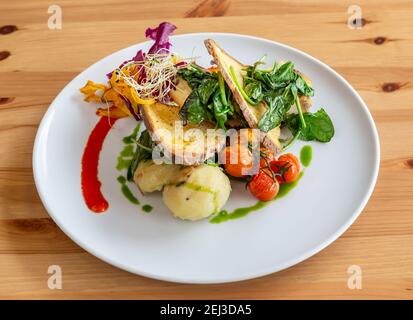 Volle vegane Mahlzeit, sehr bunt und schön dekoriert, mit Kartoffeln, Maisbrot, Tomaten und Spinat. Stockfoto