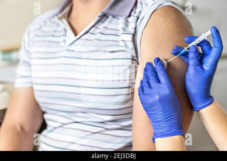 Ein Arzt impft einen Mann gegen Coronavirus in einer Klinik. Nahaufnahme. Das Konzept der Impfung, Immunisierung, Prävention gegen Covid-19 Stockfoto