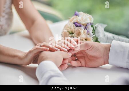 Der Bräutigam hält die Hände der Braut. Der junge Mann gab seinem geliebten Mädchen einen Blumenstrauß. Stockfoto