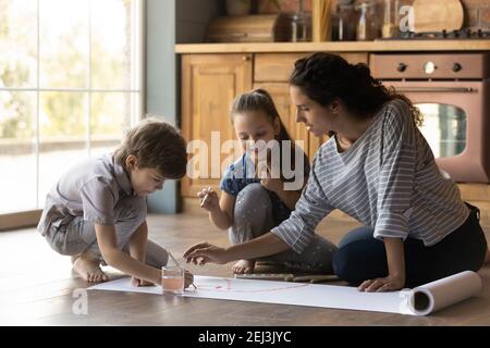 Fürsorgliche Mutter und kleine Kinder malen Aquarelle zu Hause zusammen Stockfoto