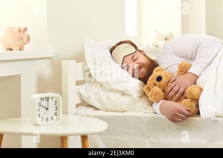 Erwachsener Mann liegt im bequemen Bett, kuschelt Teddybär und träumt süße Träume Stockfoto