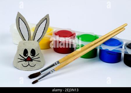 Osterhase aus Pappeibecher neben Pinsel und bunten Acryl-Bastelfarben. Weißer Hintergrund Stockfoto