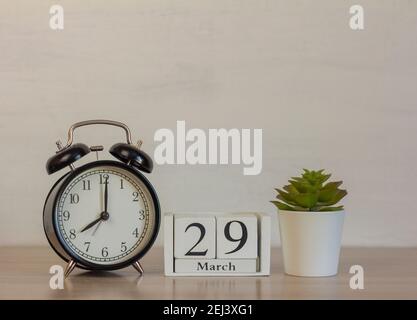 März 29 auf einem Holzkalender neben dem Wecker.Kalenderdatum, Feiertagsveranstaltung oder Geburtstag. Stockfoto