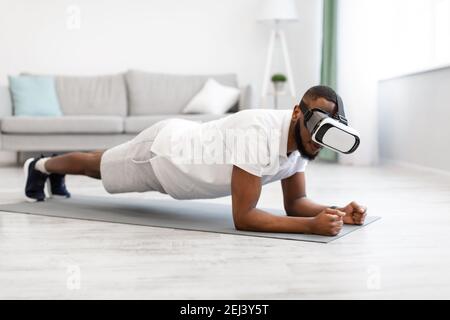Schwarzer Mann mit VR-Brille steht in Plank zu Hause Stockfoto