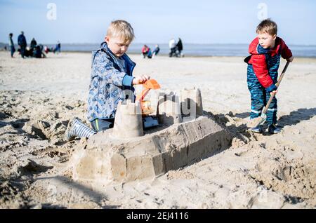 Dangast, Deutschland. Februar 2021, 21st. Die Geschwister Noah (l) und Emil bauen bei sonnigem Wetter eine Sandburg am Strand. Quelle: Hauke-Christian Dittrich/dpa/Alamy Live News Stockfoto