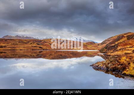 Beacon Tarn in den Blawith Fells mit den schneebedeckten Bergen in der Ferne, Lake District, England Stockfoto