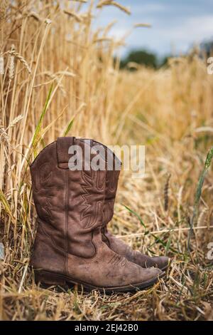 Cowboy Stiefel im landwirtschaftlichen Bereich. Alte abgenutzte Lederstiefel im Freien. Retro-Stil Stillleben von Schuhen Stockfoto