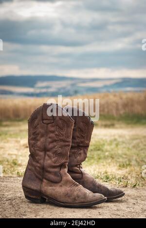 Cowboy Boot in ländlicher Szene mit launischen Himmel. Alte braune Lederstiefel im Freien. Wilder Westen im Retro-Stil Stockfoto