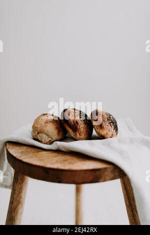 Drei Sauerteig-Brötchen mit Mohn und Sesam auf einer Serviette auf einem Holzhocker. Stockfoto