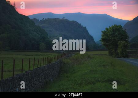 Farbenprächtiger Sonnenuntergang oder Sonnenaufgang Himmel über einer Landstraße und alte Steinmauer in englischer Landschaft in der Nähe von Grasmere im Lake District, Cumbria, E Stockfoto