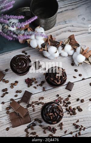 Mehrere Muffins oder Cupcakes mit schokoladenförmiger Sahne am weißen Tisch. Festliche Kerze brennt auf einem Schokoladenkuchen. Es gibt Schokolade Chips verstreut Stockfoto