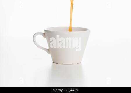 Kaffee wird von oben in einen weißen Becher gegossen, der auf einer weißen Oberfläche und einem weißen Hintergrund isoliert ist. Stockfoto