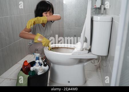 Frau trägt leider Handschuhe über ihrer Nase und reinigt die stinkende Toilette Im Badezimmer Stockfoto