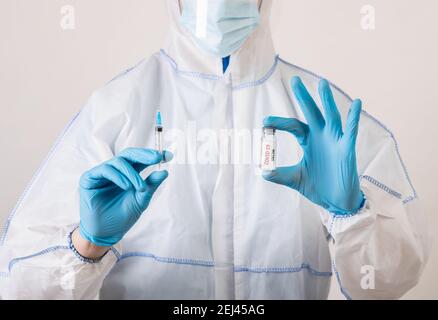 Medizinische Arbeiter in Gefahrgut Anzug, Maske und Gummihandschuhe halten covid-19-Impfstoff und Spritze auf hellem Hintergrund Stockfoto