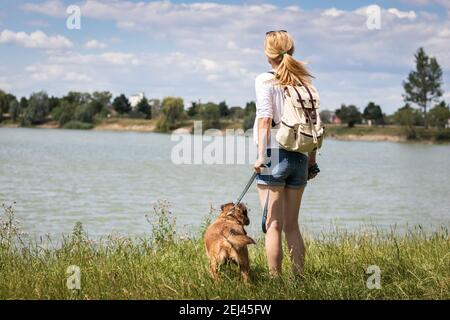 Haustierbesitzerin mit ihrem Hund, der im Sommer den Blick auf den See genießt. Frau und Mischlingshund auf dem Spaziergang. Stockfoto