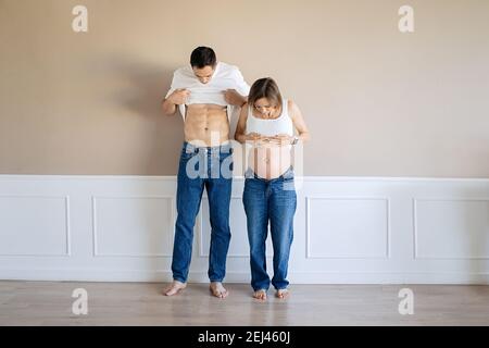 Schwangere Frau und liebevoller Ehemann zeigen sich gegenseitig ihre Bäuche Stockfoto