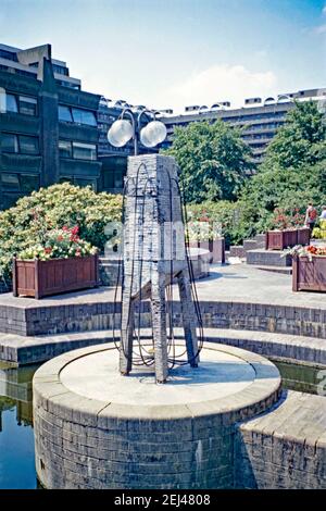 Eine Skulptur, die im Barbican Centre, London, England, UK 1993 installiert wurde. Dieses Stück trägt den Titel ‘You Fill my Head’ und ist von dem Künstler Tom Yuill. Sie befindet sich über einem Wasserbrunnen – vermutlich, als ein Ventil eingeschaltet wurde, bildete die Skulptur ein Wasserspiel. Dies war Teil der ‘Art in the City’ von 1993 und zielte darauf ab, Skulpturen zwischen den Grünflächen und der unverwechselbaren Architektur der City of London zu setzen. Ein ähnliches Schema, ‘Sculpture in the City’, begann 2011 mit Kunstwerken international anerkannter und aufstrebender Künstler, die jeden Sommer zu sehen waren – ein Vintage-Foto aus den 1990er Jahren. Stockfoto