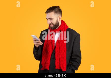 Glücklicher Geschäftsmann in formellen Anzug und roten Schal mit Smartphone, mit Online-Geschäftsanruf auf orangenen Hintergrund Stockfoto