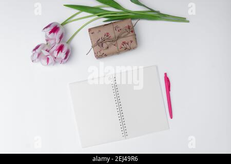 Draufsicht auf Tulpen, Geschenk und leeren Notizblock auf weißem Hintergrund Stockfoto